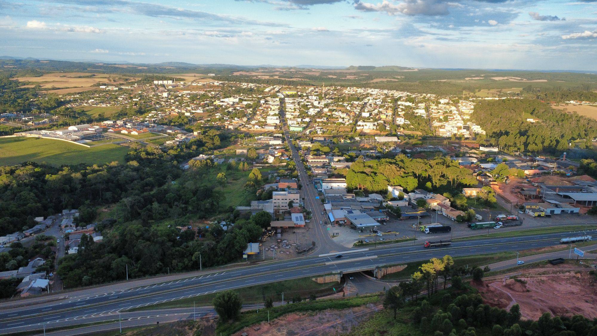 Vista aérea de Ortigueira (PR): a rodovia em primeiro plano e o acesso principal levando à área urbana do município